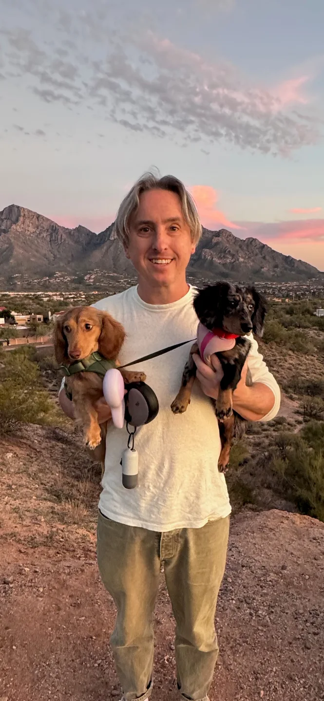 David holding Arthur and Stowe on a desert trail beneath a pink sunset